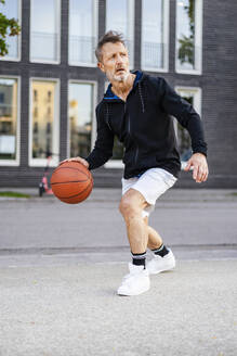 Sportler dribbelt Basketball und spielt auf einem Sportplatz - DIGF20896