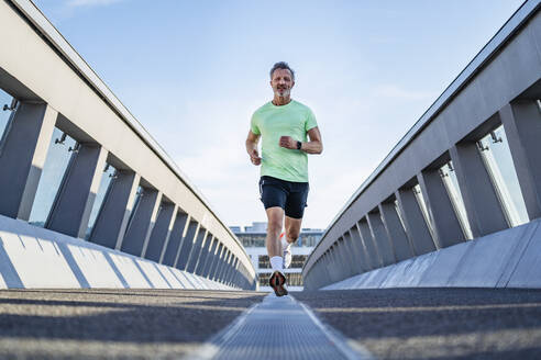 Mature athlete jogging on footbridge - DIGF20936