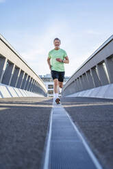 Älterer Sportler joggt auf dem Steg vor dem Himmel - DIGF20937