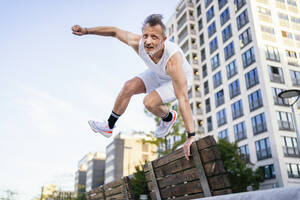 Aktiver Sportler springt über eine Bank in der Stadt - DIGF20948