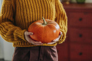 Woman wearing sweater and holding pumpkin at home - VSNF01406