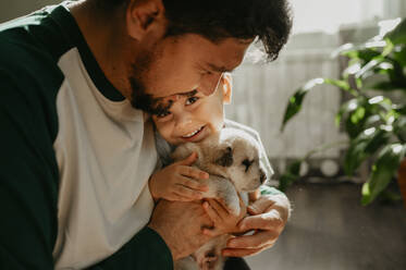 Smiling man holding son and cute puppy at home - ANAF02268