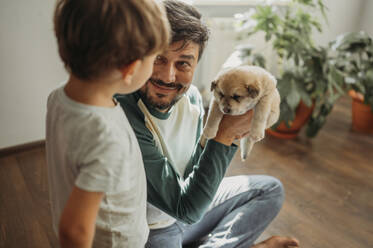Lächelnder Mann zeigt seinem Sohn zu Hause ein süßes Hündchen - ANAF02289