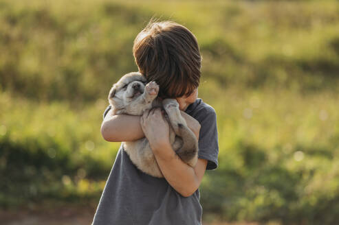 Junge umarmt niedlichen Mischlingswelpen auf der Wiese - ANAF02294