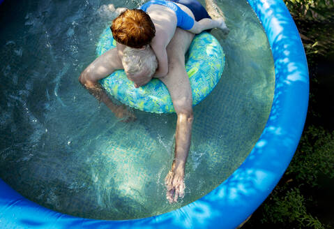 Großvater und Enkel schwimmen im Planschbecken im Garten - MBLF00002