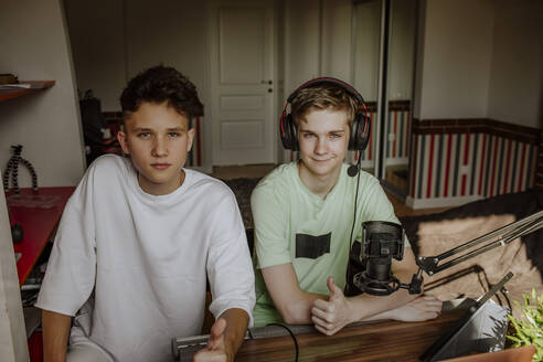 Teenage boys podcasting and showing thumbs up sign at home - MDOF01606