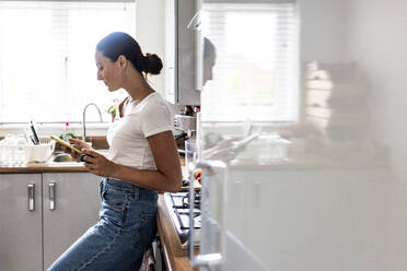 Frau benutzt Mobiltelefon in der Küche zu Hause - WPEF07726