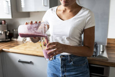 Frau gießt gesunden Milchshake in Glas zu Hause - WPEF07737