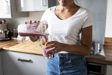 Woman pouring healthy milkshake in glass at home - WPEF07737