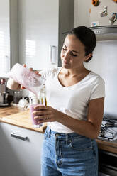 Frau gießt Milchshake in Glas zu Hause - WPEF07739