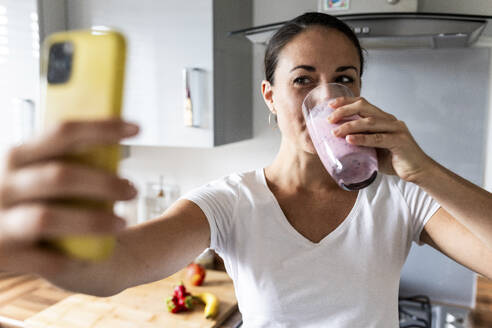 Woman drinking milkshake and clicking selfie through smart phone - WPEF07742