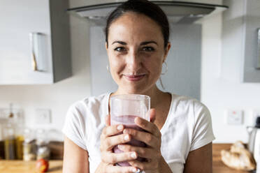 Happy woman holding glass of milkshake at home - WPEF07745