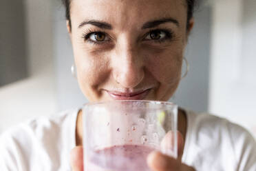 Smiling woman holding glass of milkshake at home - WPEF07746