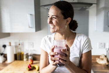 Cheerful woman holding glass of milkshake at home - WPEF07747