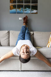 Happy woman lying on sofa with eyes closed at home - WPEF07769