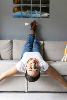 Happy woman lying on sofa with eyes closed at home - WPEF07769