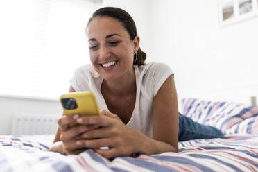 Glückliche Frau mit Smartphone auf dem Bett zu Hause - WPEF07780
