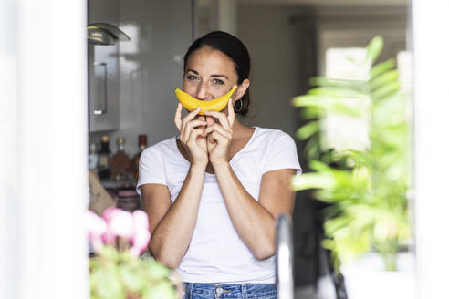 Woman holding banana over mouth at home - WPEF07786