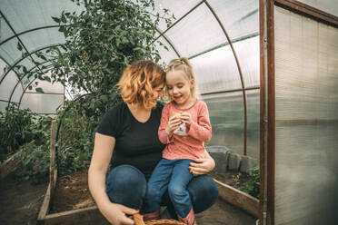 Lächelnde Mutter mit Tochter, die Obst im Gewächshaus hält - ADF00204