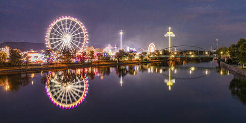 Germany, Baden-Wurttemberg, Stuttgart, Cannstatter Wasen, Panoramic view of glowing Ferris Wheel reflecting in Neckar river at night - WDF07415