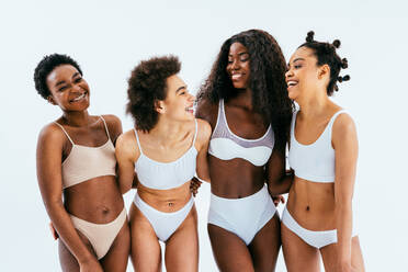 Four smiling women of different ages embracing their natural and aging  bodies. Four happy and body positive women embracing each other while  wearing red underwear against a studio background. stock photo