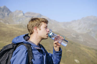 Blonder Mann trinkt Wasser aus einer Flasche in der Nähe eines Berges - NJAF00584