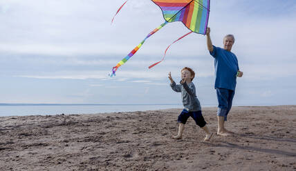 Grandson flying kite with grandfather at beach - MBLF00020