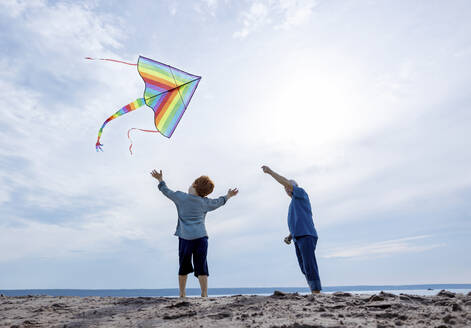 Boy standing with grandfather flying kite at beach - MBLF00024