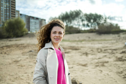 Lächelnde Frau mit lockigem Haar am Strand stehend - ANAF02305