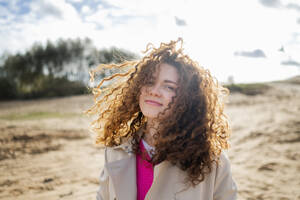 Lächelnde Frau mit lockigem Haar am Strand stehend - ANAF02306