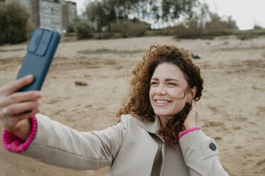 Smiling woman taking selfie with smart phone at beach - ANAF02309