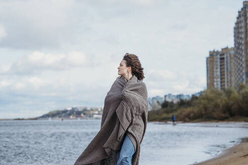 Frau in Schal eingewickelt, die am Strand unter dem Himmel spazieren geht - ANAF02315