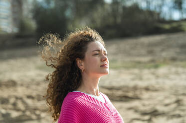 Junge Frau mit lockigem Haar am Strand - ANAF02317