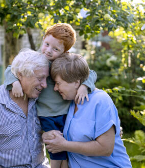 Junge, der seine Großeltern im Garten umarmt - MBLF00030