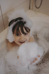 Boy playing with soap sud in bathtub at home - ANAF02332