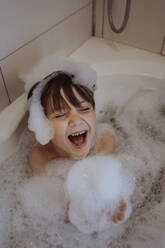 Cheerful boy with soap sud in bathtub at home - ANAF02333