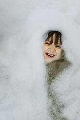 Fröhlicher Junge inmitten von Seifenlauge in der Badewanne - ANAF02335
