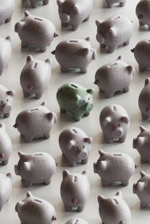 Green piggy bank amidst many piggy banks over white background - GCAF00455