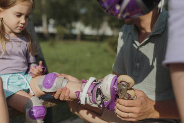 Vater hilft seiner Tochter beim Anbringen von Rollschuhen im Park - LLUF01099