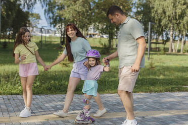 Lächelndes Mädchen beim Rollschuhlaufen mit Eltern und Schwester im Park - LLUF01100