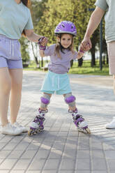 Lächelndes Mädchen, das mit seinen Eltern auf dem Fußweg im Park Rollschuh läuft - LLUF01101