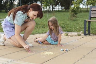 Mutter bringt ihrer Tochter das Zeichnen auf dem gefliesten Boden im Park bei - LLUF01103