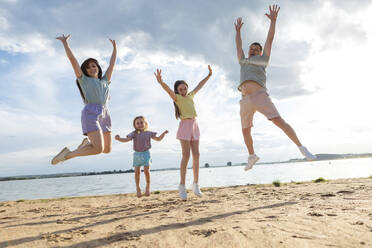 Cheerful parents with daughters jumping at beach - LLUF01109