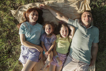 Lächelnde Eltern mit Töchtern auf einer Decke im Park liegend - LLUF01111