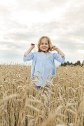 Happy girl touching hair standing in field - LLUF01113