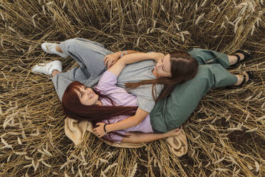 Smiling mother and daughter lying amidst field - LLUF01118