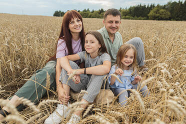 Smiling parents with daughters sitting amidst field - LLUF01121