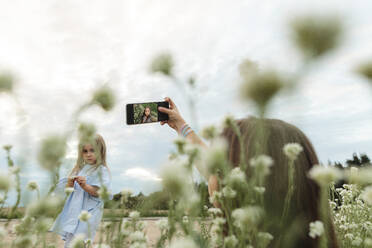 Woman clicking selfie through smart phone in front of girl standing at field - LLUF01123