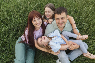 Happy parents with daughters sitting and having fun in field - LLUF01125