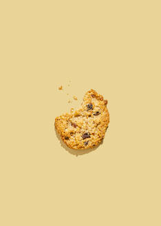 Raisin cookie with missing bite against yellow background - FLMF01031